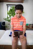 Smiling boy using digital tablet while sitting on bed