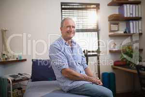 Portrait of smiling senior male patient sitting on bed