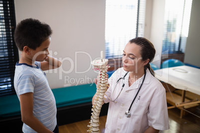 Boy looking at female therapist explaining with artificial spine