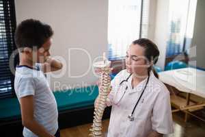 Boy looking at female therapist explaining with artificial spine