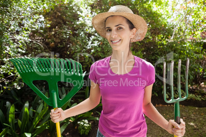 Portrait of smiling beautiful woman holding gardening fork and rake