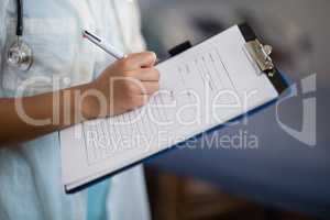 Midsection of female doctor writing on clipboard
