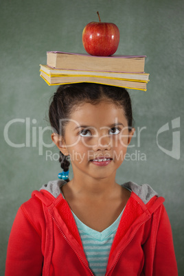 Young girl balancing books and apple on her head