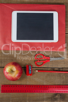 Apple, digital tablet and school supplies on wooden table