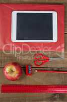 Apple, digital tablet and school supplies on wooden table
