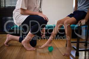 Low section of female therapist kneeling by boy stepping on stress ball