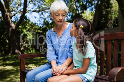 Grandmother and granddaughter holding hands while sitting on bench