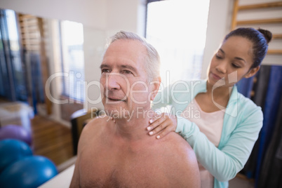 Shirtless senior male patient receiving neck massage from female therapist