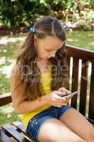 Girl using mobile phone while sitting on wooden bench