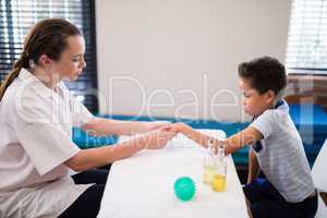 Side view of female therapist examining hand while boy sitting at table