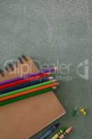 Color pencils, crayons, push pins and book on chalkboard