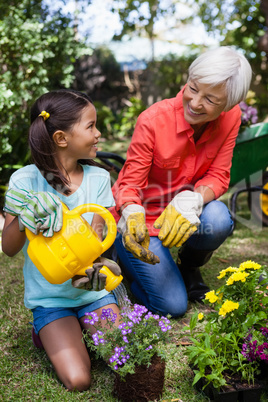 Cheerful senior woman looking at girl watering flowers