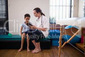 Female doctor showing digital tablet to boy against wall