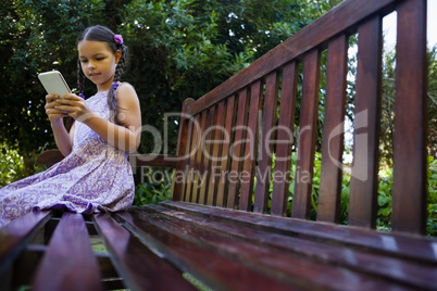 Surface level of girl sitting on wooden bench while using mobile phone