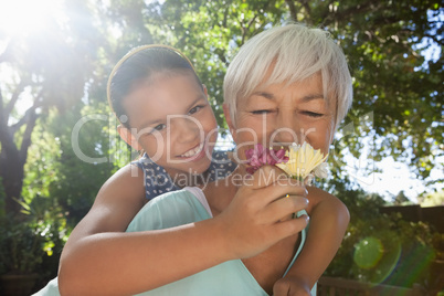 Grandmother smelling flowers while piggybacking granddaughter