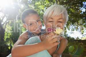 Grandmother smelling flowers while piggybacking granddaughter