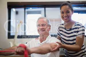 Portrait of smiling senior male patient pulling red resistance band with female doctor