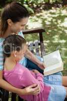 High angle view of mother reading novel to daughter on bench