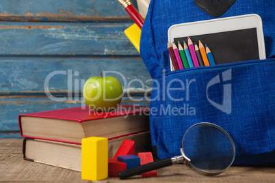 School supplies, apple, digital tablet and magnifying glass on wooden table
