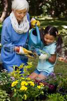 Smiling girl and grandmother watering plants