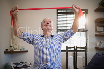Smiling senior male patient pulling red resistance band while looking up