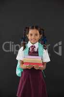 Portrait of schoolgirl in school uniform holding books against blackboard