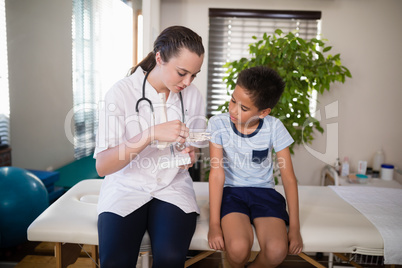 Young female therapist explaining boy with artificial bone while sitting on bed