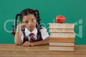 Schoolgirl sitting beside books stack with apple on top against chalkboard