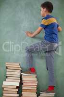 Schoolboy climbing steps of books stack