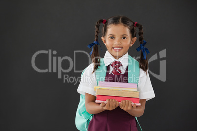 Portrait of schoolgirl in school uniform holding books against blackboard