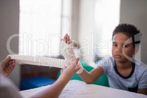Portrait of boy sitting at table while female therapist wrapping bandage on hand