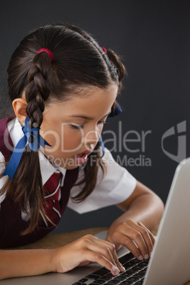 Schoolgirl using laptop against blackboard