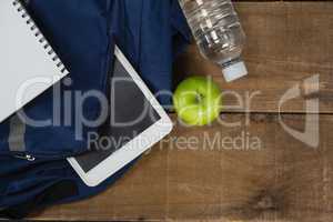Schoolbag, apple, water bottle, book and digital table on wooden table
