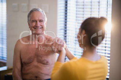 Smiling shirtless senior male patient looking at female therapist giving arm massage