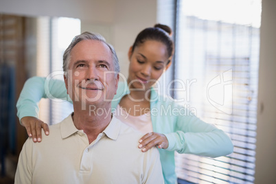 Young female therapist giving shoulder massage to senior patient