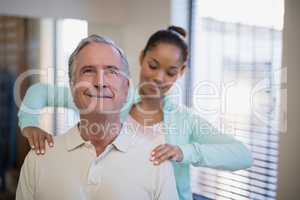 Young female therapist giving shoulder massage to senior patient