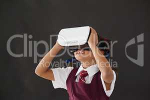 Schoolgirl using virtual reality headset against blackboard