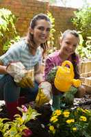 Portrait of smiling woman and daughter crouching by flowers with watering can