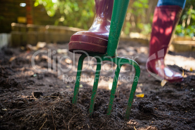 Low section of senior woman standing by garden fork on dirt