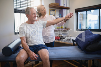 Female doctor examining wrist of senior male patient