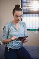 Young female therapist using digital tablet while sitting on bed