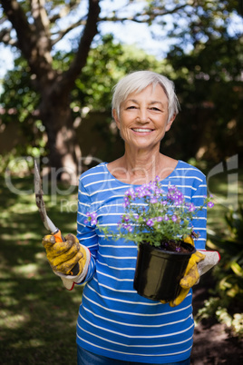 Portrait of smiling senior woman holding potted plant and trowel