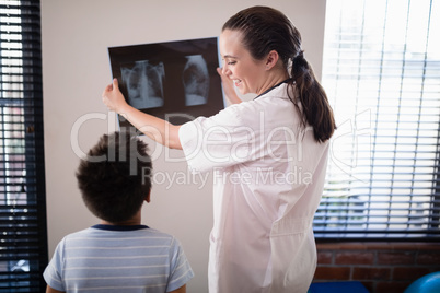 Smiling female doctor showing x-ray to boy against wall