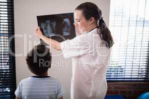 Smiling female doctor showing x-ray to boy against wall