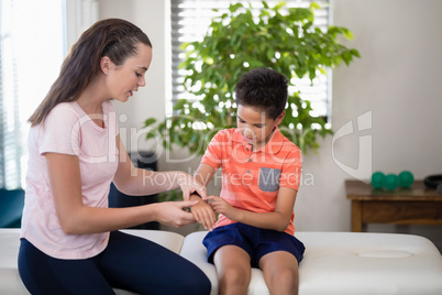 Female therapist sitting on bed with boy examining hand