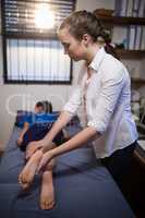 Side view of female therapist examining leg with boy lying on bed