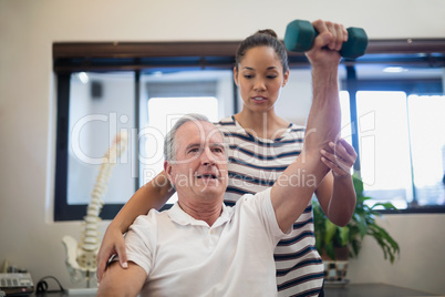 Female doctor looking at senior patient lifting dumbbell