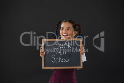 Smiling schoolgirl holding slate with text against blackboard