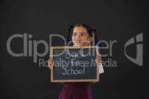 Smiling schoolgirl holding slate with text against blackboard