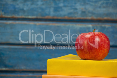 Stack of books and apple against blue wooden background